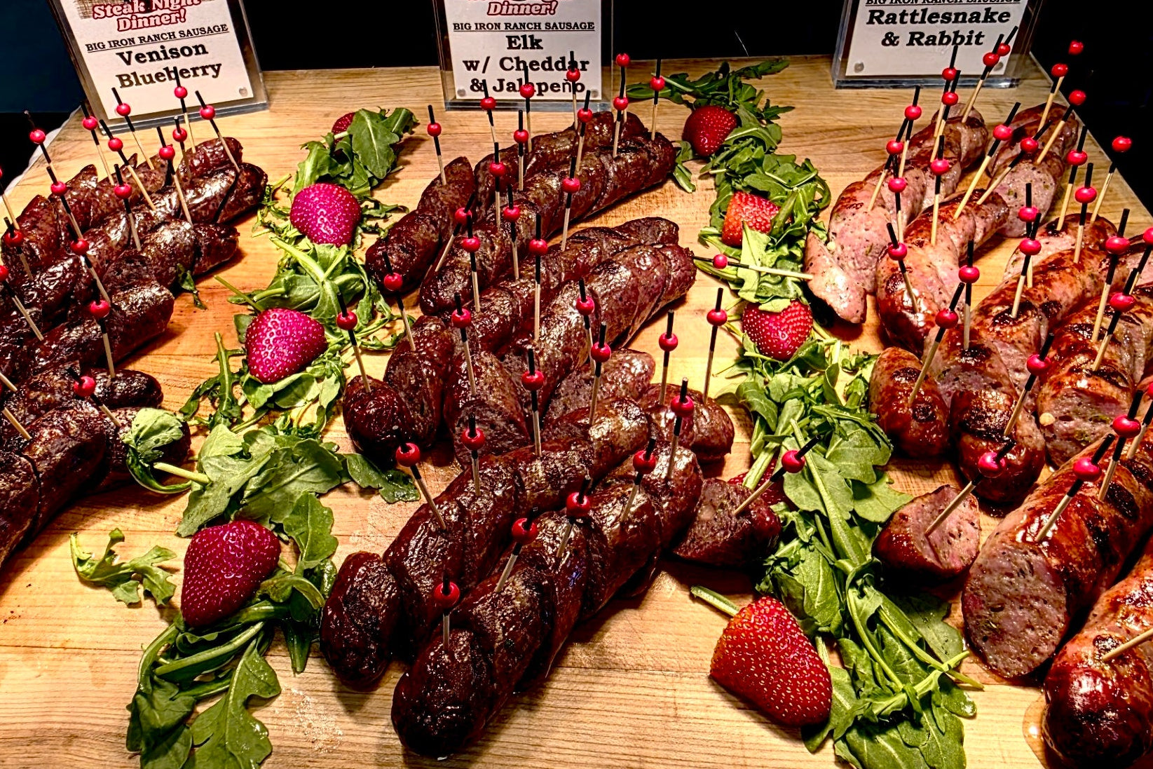 Assorted smoked wild game meats on skewers with decorative elements on a wooden board.